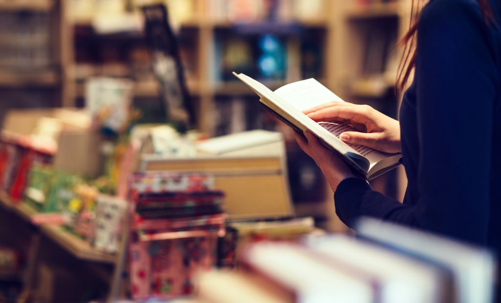 An interior image of a woman reading a book in a bookstore.