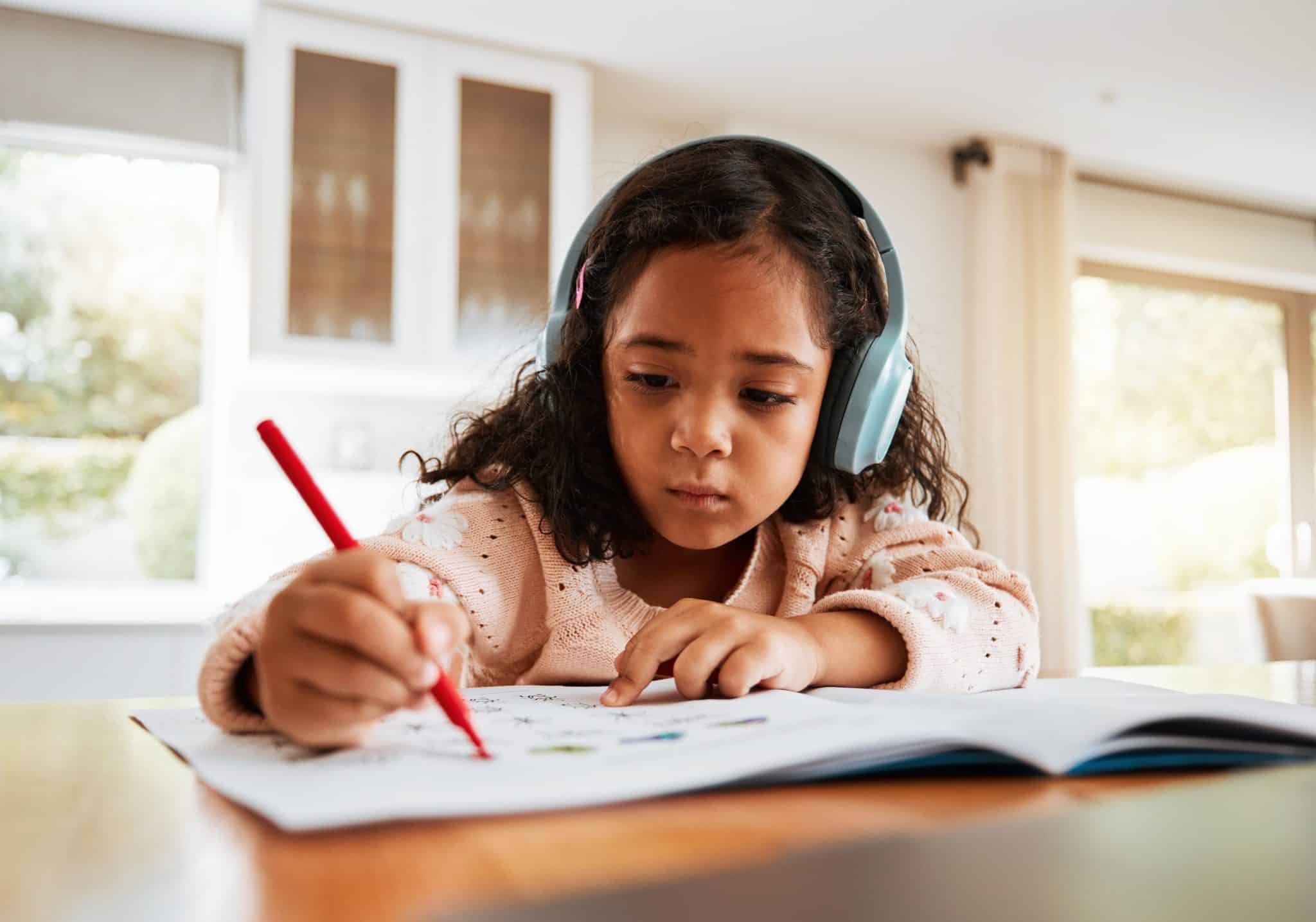 Education, learning or headphones on kid for homework, writing and drawing books for homeschooling. Childhood development, focus and young girl listening to music while studying for kindergarten test