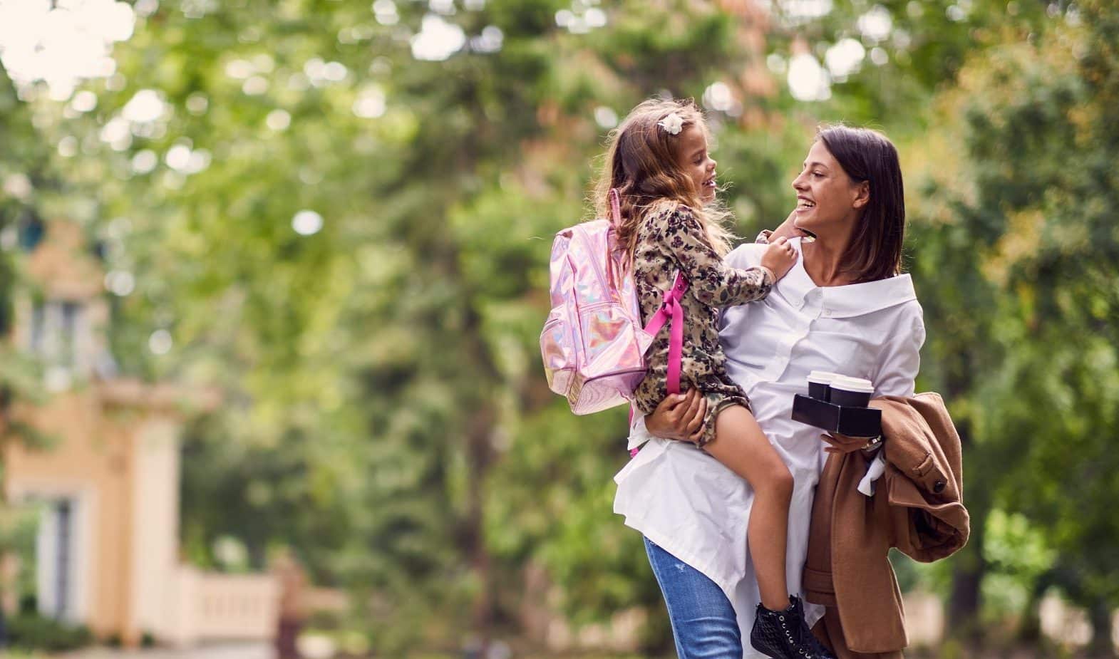 smiling mother holding a daughter with schoolbag smiling mother holding a daughter with schoolbag
