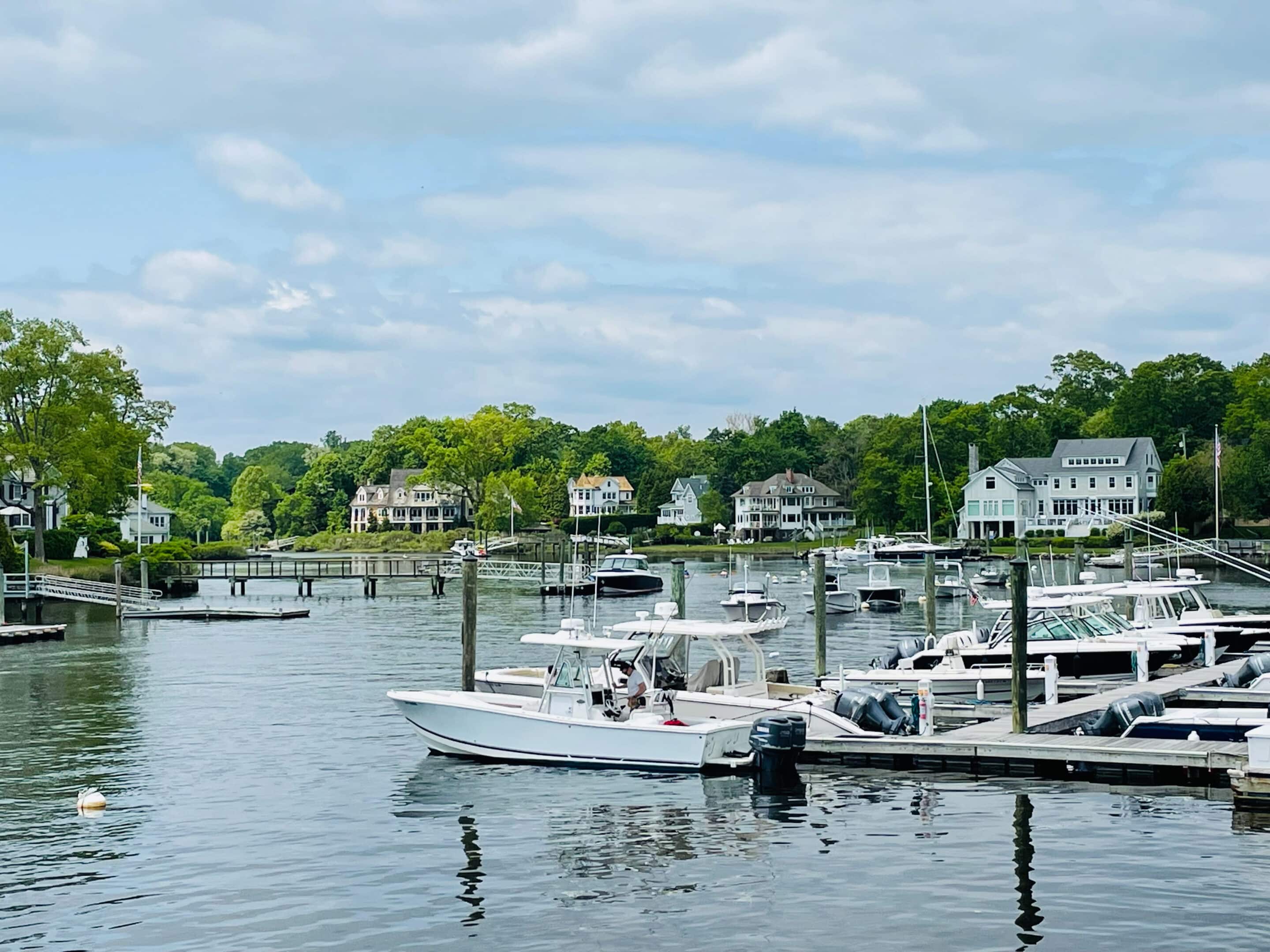 Darien CT Waterfront and Marina Boats docked along the waterfront in Darien, Connecticut, with coastal homes and trees in the background under a partly cloudy sky.