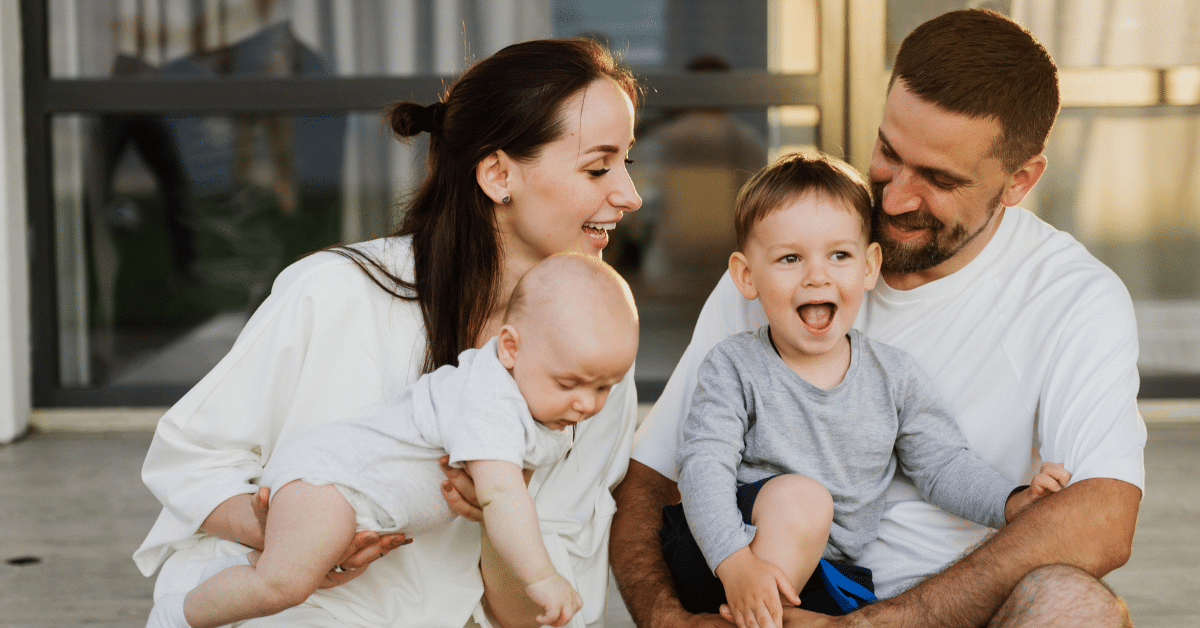 Family Moving from NYC to the Philadelphia Suburbs Family with two young children smiling together outside their new home after moving from NYC to the Philadelphia suburbs