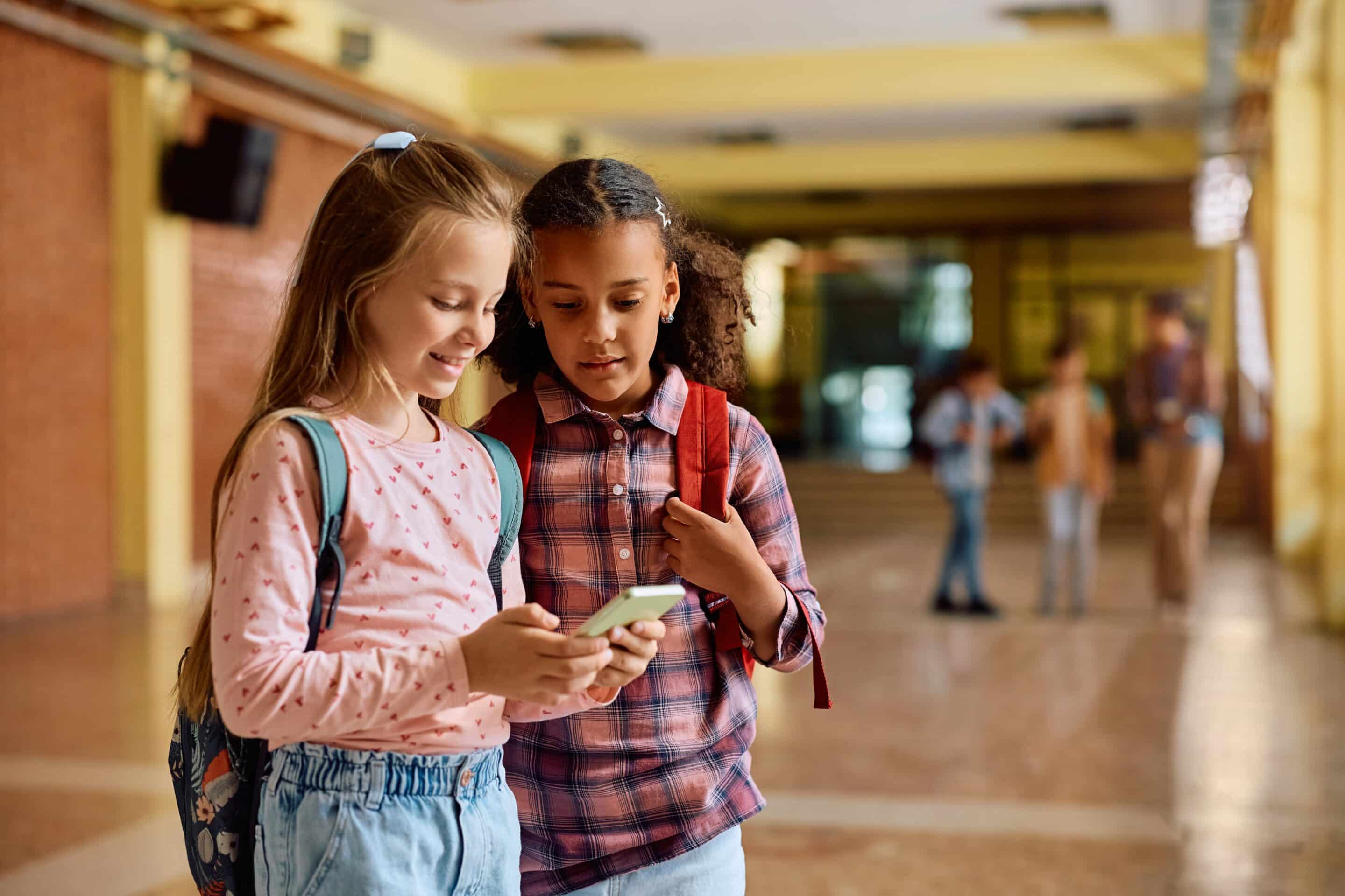 Students in a School Hallway Ahead of New Jersey’s Phone-Free Schools Law Elementary school students with backpacks looking at a phone in a school hallway, reflecting New Jersey’s phone-free schools law